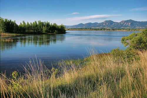 A serene lake surrounded by lush greenery and mountains under a clear blue sky.