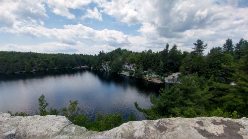 A serene lake surrounded by lush greenery and rocky cliffs under a partly cloudy sky.