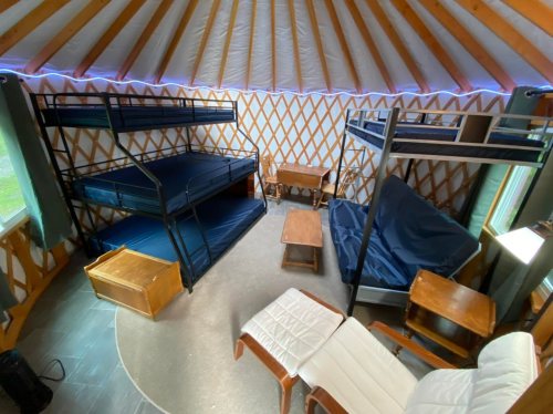 Interior of a yurt featuring bunk beds, a futon, and wooden furniture, with a cozy, spacious layout.