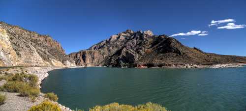 A serene lake surrounded by rocky mountains under a clear blue sky, with sparse vegetation along the shore.