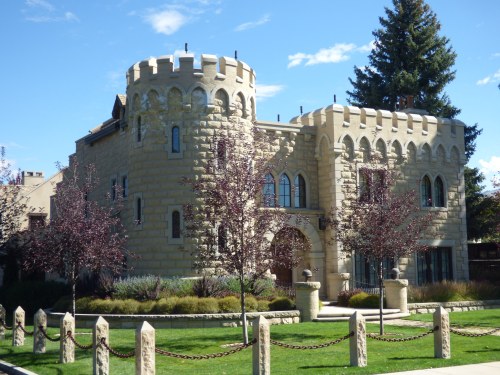 A stone castle with turrets, surrounded by trees and a manicured lawn, under a clear blue sky.