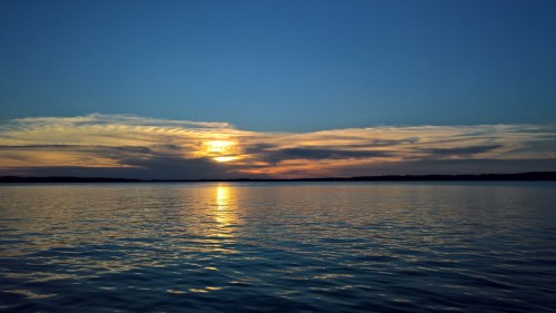 A serene sunset over a calm lake, with colorful clouds reflecting on the water's surface.