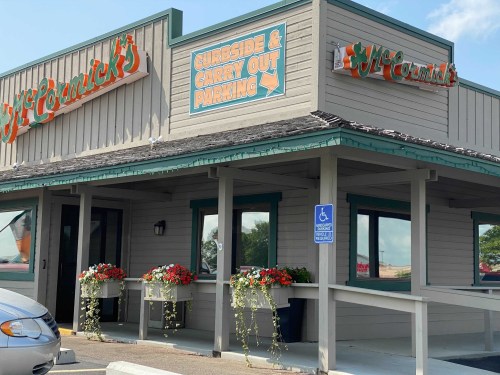 Exterior of McCormick's restaurant with signs for curbside and carryout parking, featuring flower planters and a blue sky.