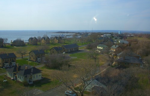 A coastal view featuring houses, trees, and a distant harbor under a clear sky.