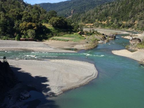 A scenic view of a river winding through green hills and rocky banks under a clear blue sky.