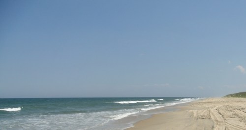 A serene beach scene with gentle waves, a clear blue sky, and sandy shore stretching into the distance.