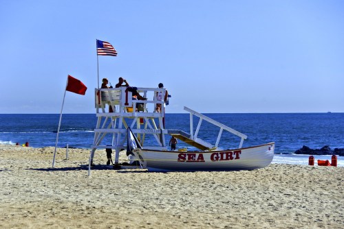 Lifeguard tower on a sandy beach with an American flag, overlooking the ocean on a clear day.
