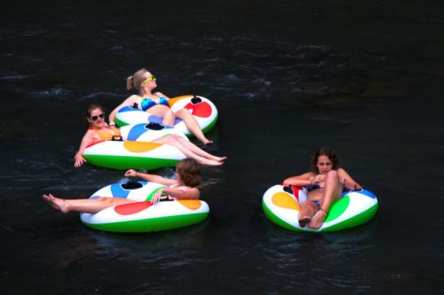 Four people relax on colorful inner tubes in a river, enjoying a sunny day.