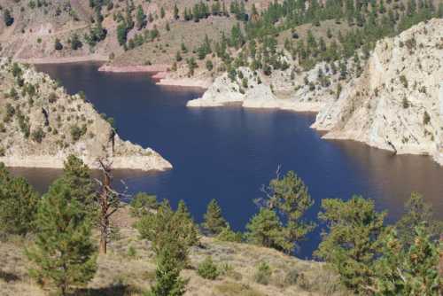 A serene lake surrounded by rocky cliffs and lush greenery, reflecting the clear blue sky.