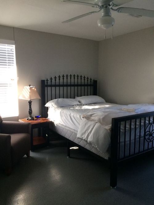 A cozy bedroom featuring a black metal bed, a chair, a lamp, and a small bedside table with items on it.