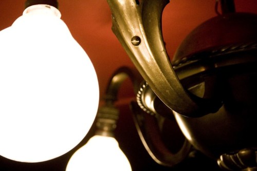 Close-up of a vintage chandelier with glowing light bulbs against a dark red background.