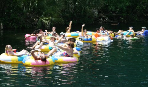 A group of people relaxes on colorful inner tubes in a serene, green river, enjoying a sunny day.