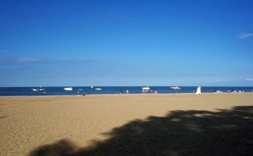 A sandy beach with boats on the water and a clear blue sky, creating a serene coastal scene.