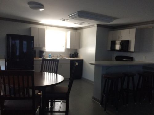 A dimly lit kitchen with a round table, chairs, and modern appliances, including a refrigerator and microwave.