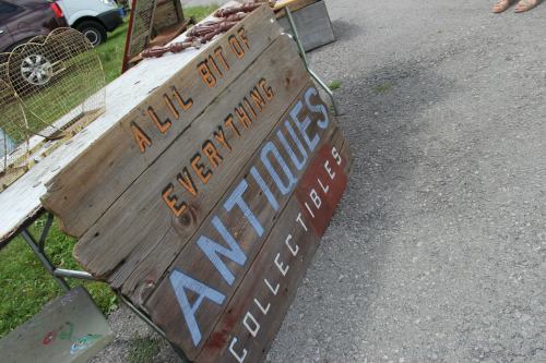 A wooden sign reading "A Lil Bit of Everything" and "Antiques Collectibles" at a market stall.
