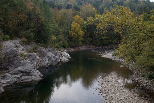 A serene river winding through a forested landscape with autumn foliage and rocky banks.