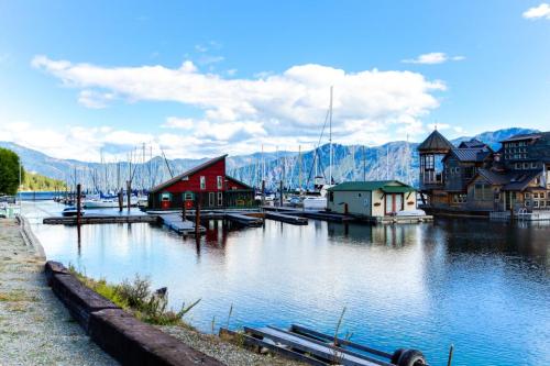 A serene marina scene with colorful buildings, boats, and mountains under a blue sky with fluffy clouds.