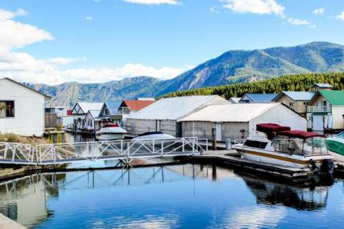 A serene marina with boats, colorful houses, and mountains under a clear blue sky.