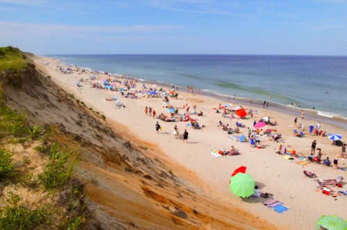 A sunny beach scene with people sunbathing, colorful umbrellas, and gentle waves along the shore.