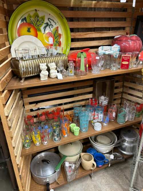 A wooden shelf displaying various kitchen items, including plates, glasses, and decorative containers.