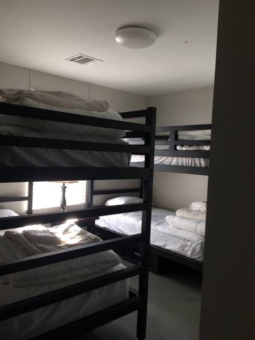 A small room with two sets of bunk beds, neatly made with white bedding, and a lamp on a nightstand.
