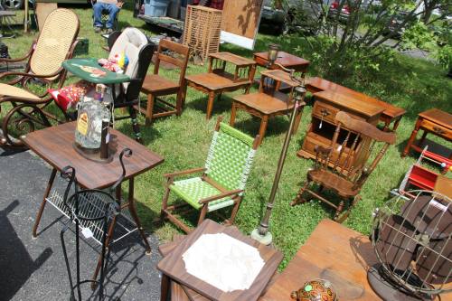 A variety of vintage furniture, including chairs and tables, displayed outdoors on grass at a flea market.