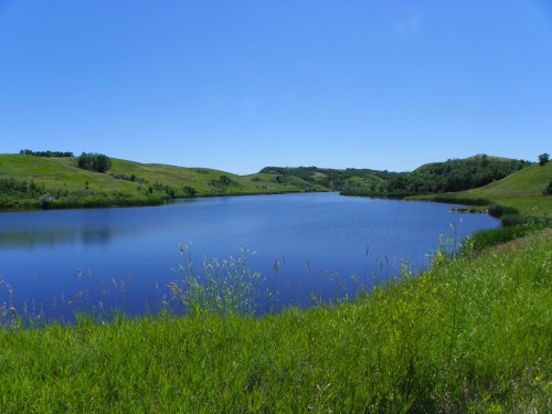 A serene lake surrounded by lush green hills under a clear blue sky.