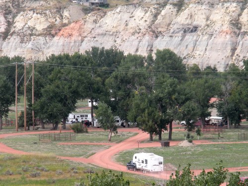A scenic view of a campground with RVs, surrounded by trees and rocky cliffs in the background.