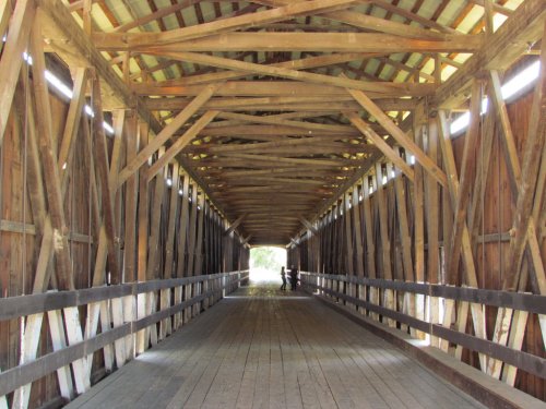Interior view of a wooden covered bridge, featuring exposed beams and a pathway leading to light at the far end.