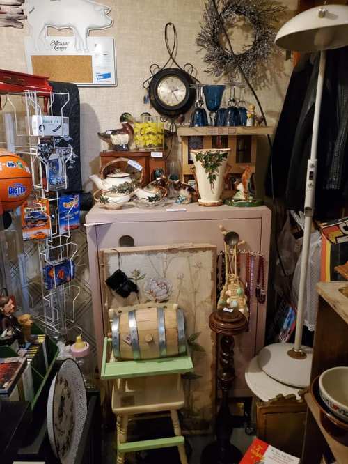 A cluttered antique shop display featuring various vintage items, including a clock, figurines, and decorative pieces.