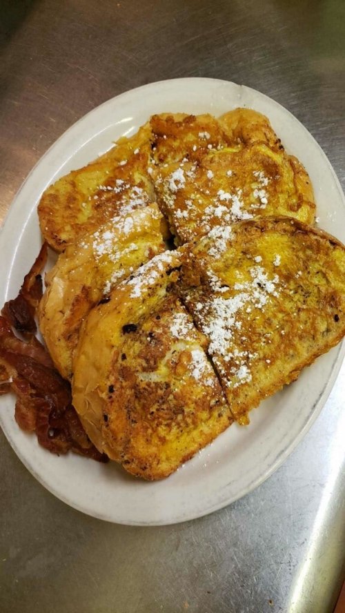 A plate of golden-brown French toast dusted with powdered sugar, served with crispy bacon on the side.