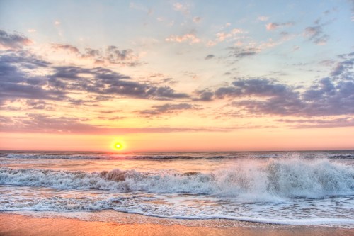 A serene beach scene at sunset, with waves crashing and a colorful sky filled with clouds.