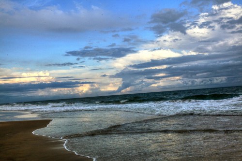 A serene beach scene with gentle waves, sandy shore, and a dramatic sky filled with clouds.