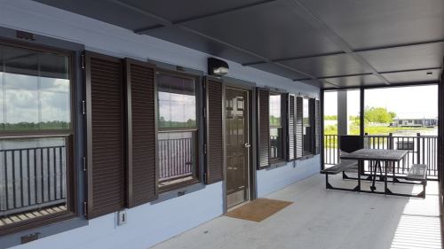 A spacious porch with brown shutters, a door, and a picnic table overlooking a green landscape.