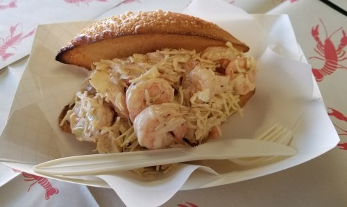 A toasted sandwich filled with shrimp and creamy coleslaw, served on a paper tray with a plastic fork.