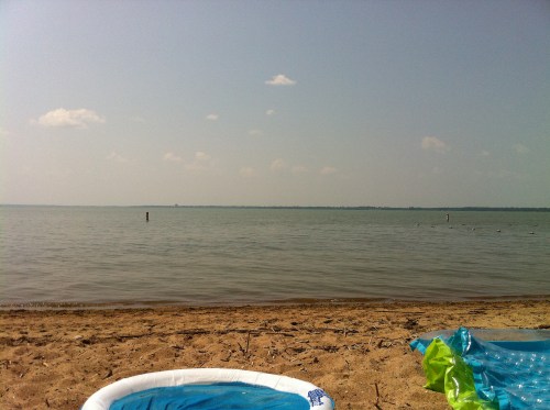 A serene beach scene with calm water, sandy shore, and a clear sky dotted with a few clouds.