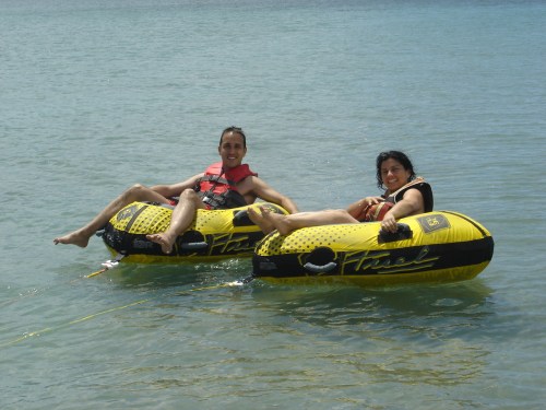 Two people relax on yellow inflatable tubes in calm water, enjoying a sunny day at the beach.