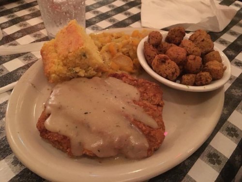 A plate of fried chicken with gravy, cornbread, okra, and a side of mixed vegetables on a checkered tablecloth.