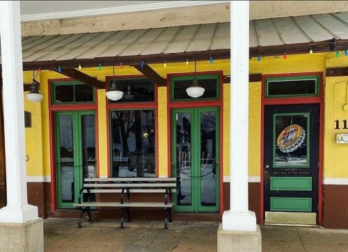 Colorful storefront with green doors and windows, yellow walls, and a bench outside, decorated with string lights.