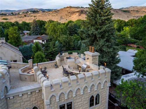Aerial view of a castle-like structure with a rooftop terrace, surrounded by trees and hills in the background.