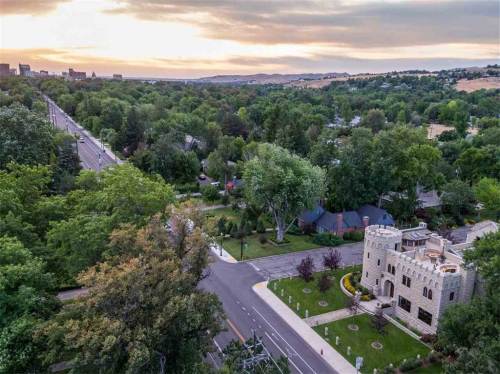 Aerial view of a castle-like building surrounded by trees and a road, with a sunset in the background.