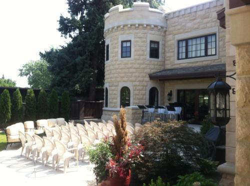A stone castle-like building with a patio, surrounded by chairs and lush greenery in a sunny outdoor setting.