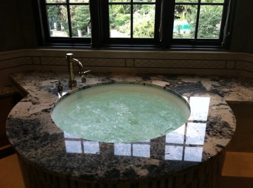 A round, bubbling hot tub on a granite countertop, with large windows overlooking greenery outside.