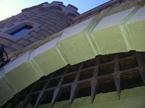 A close-up view of a stone archway with pointed metal spikes, leading to a castle-like structure.