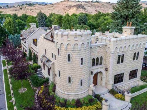 Aerial view of a castle-like house surrounded by lush greenery and colorful flowers.