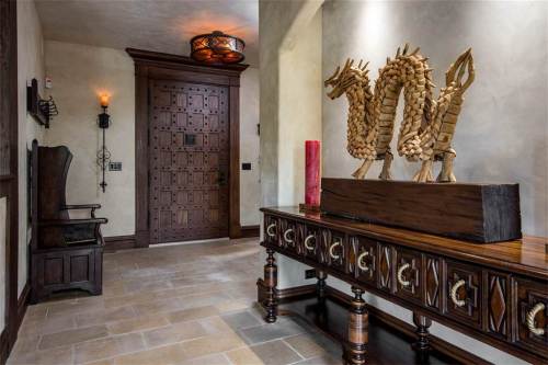 A spacious hallway features a wooden dragon sculpture, ornate console table, and a large wooden door.