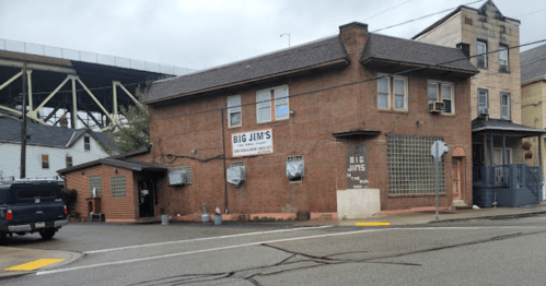 A brick building with a sign reading "Big Jim's," located at a street corner under a cloudy sky.