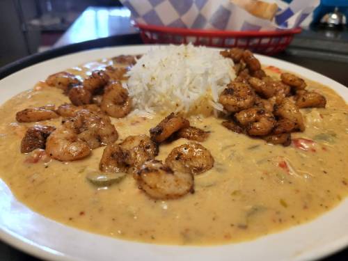 A plate of shrimp in creamy sauce with rice, garnished with spices and served with a side of bread in a basket.