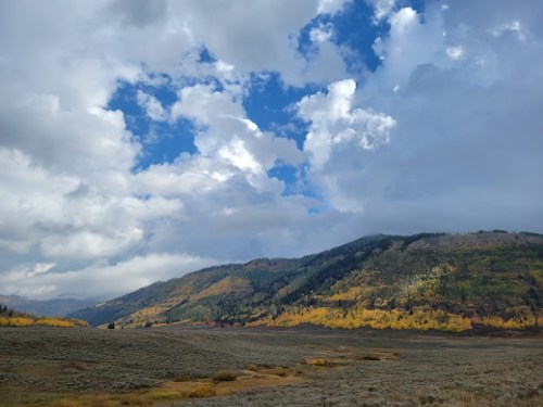 A scenic landscape featuring rolling hills, colorful autumn trees, and a cloudy blue sky.