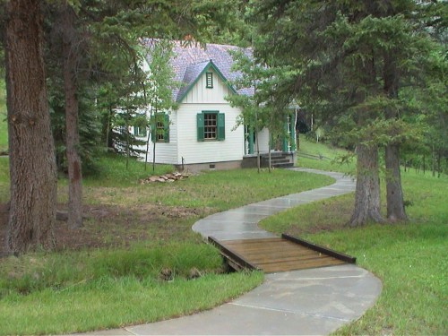 A charming white house with green shutters, surrounded by trees and a winding path leading to it.